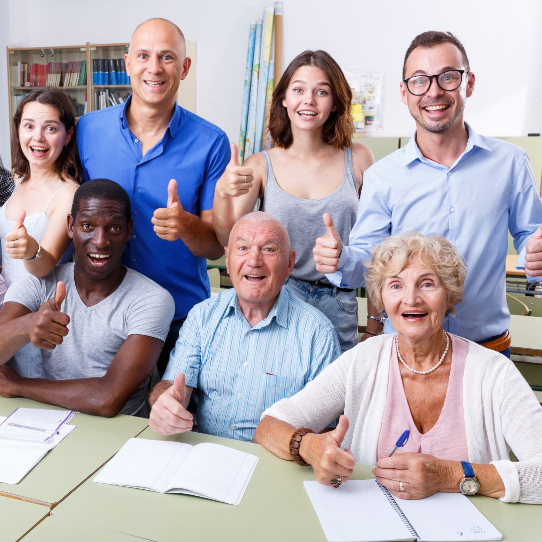 Group of people of all ages in a room giving a thumbs up sign